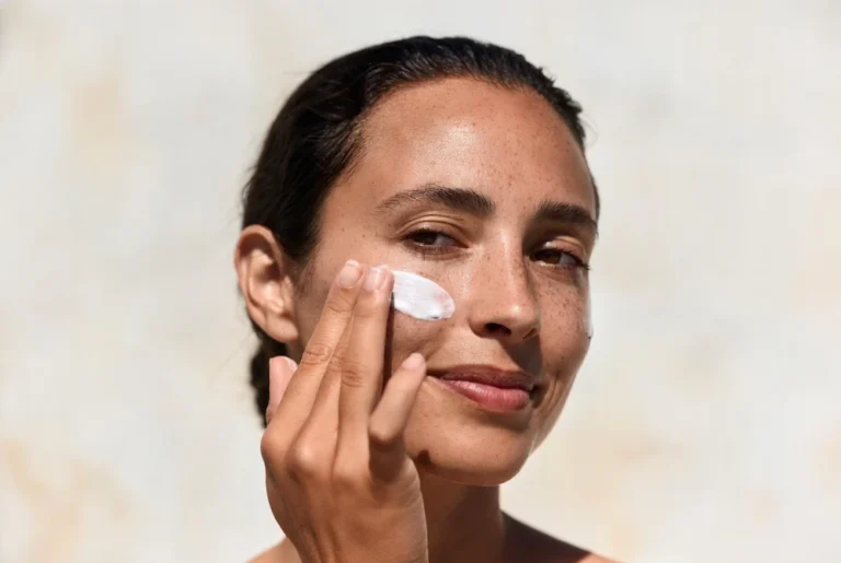 mujer aplicando bloqueador dermatológico en el rostro con piel saludable y uniforme