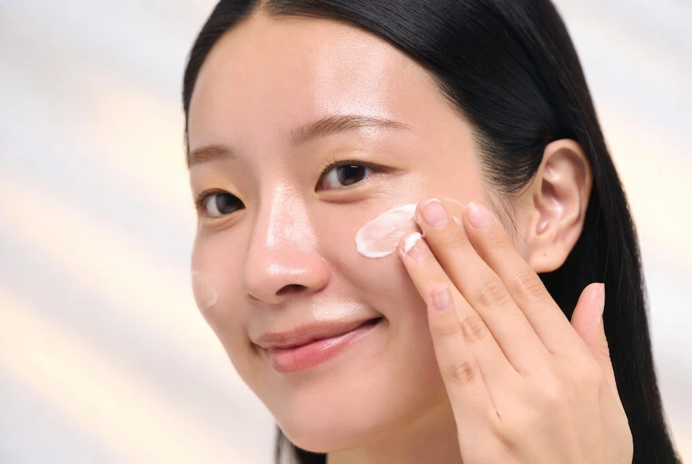 mujer asiática aplicando crema coreana hidratante sobre piel luminosa y saludable