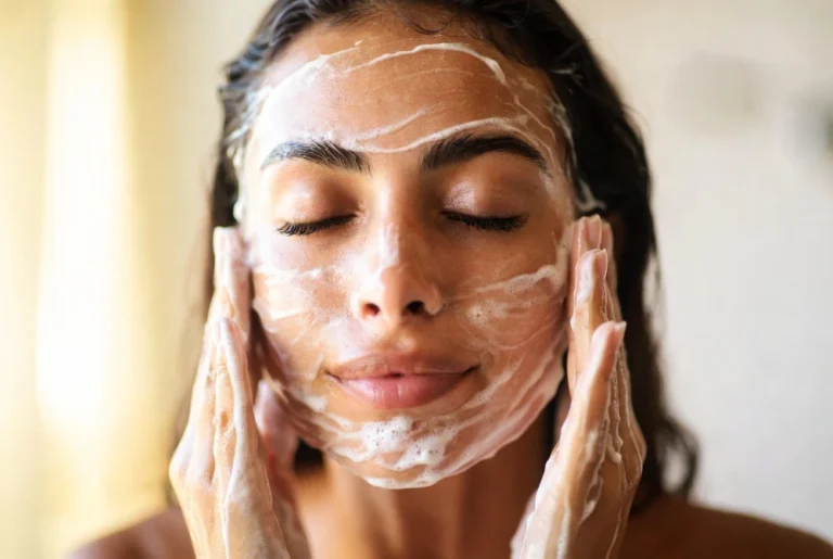 mujer latina lavándose la cara con jabón facial suave y espuma cremosa