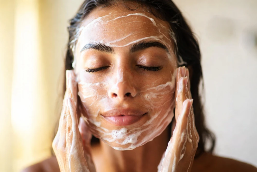 mujer latina lavándose la cara con jabón facial suave y espuma cremosa